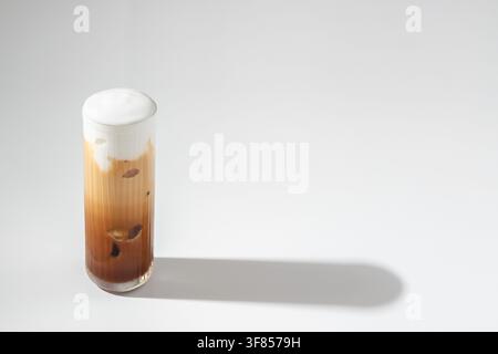 Caffè freddo con schiuma cremosa in un bicchiere alto su sfondo bianco con ombra lunga Foto Stock