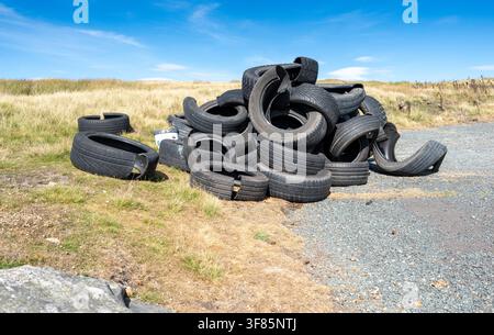 Cumulo di vecchi pneumatici per auto abbandonati su un lato della strada rurale nelle Yorkshire Dales, causando un rischio di inquinamento. Foto Stock