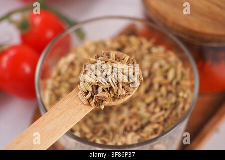 Semi di finocchio in un cucchiaio di legno vicino a pomodori freschi Foto Stock