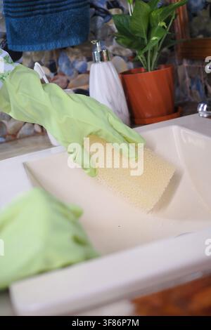 Pulizia di un lavandino con una spugna e guanti in una cucina Foto Stock
