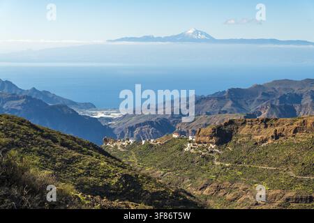 Vista del Roque Bentayga che si erge sopra il paesaggio montuoso aspro di Tejeda con vedute lontane del Monte Teide sotto un cielo blu limpido a Tejeda, Canarie Foto Stock