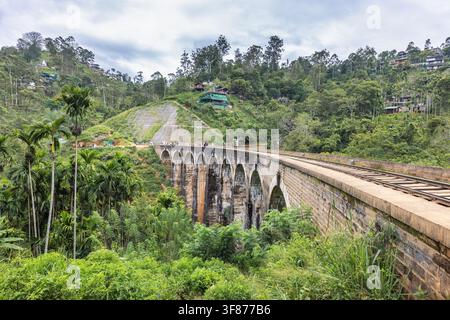Ponte delle Nove Arche vicino alla città di Ella nello Sri Lanka. Antica ponte ad arco in pietra con binari ferroviari che si snodano attraverso montagne verdi e lussureggianti sotto un cielo nuvoloso Foto Stock