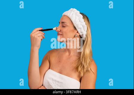 Donna che applica polvere di trucco sul naso usando un pennello cosmetico Foto Stock