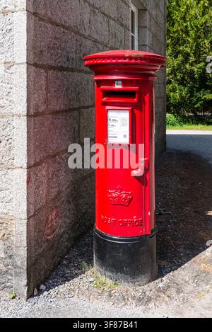 Royal Deeside, Scozia, Regno Unito – 16 luglio 2025: Una tradizionale cassetta postale rossa presso il Balmoral Castle Estate, circondata da architettura in pietra e vegetazione Foto Stock