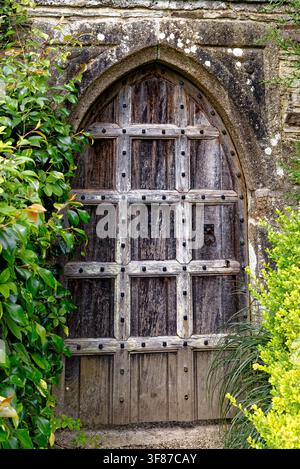 Una porta storica in quercia splendidamente incorniciata e consumata dal tempo, inserita in una cornice in pietra ad arco, incastonata tra siepi rigogliose verdi e gialle del giardino a Lanhydrock H Foto Stock