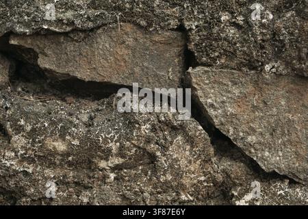 Vista macro di un muro in pietra naturale eroso. Toni terrosi scuri e trame ruvide per sfondi. Foto Stock