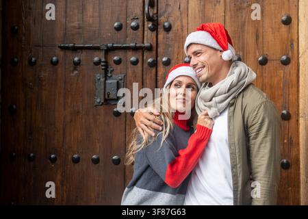 Coppia sorridente con cappelli da Babbo Natale e vestiti caldi mentre godono del Natale insieme all'aperto in città. Foto Stock