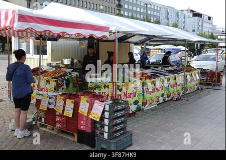 Un vivace banco di mercato locale a Lahti, in Finlandia, pieno di verdure fresche, bacche e prodotti regionali sotto una tenda blu e bianca. Foto Stock