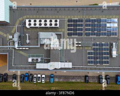 Vista aerea dall'alto di un tetto commerciale con pannelli solari e unità di raffreddamento HVAC accanto a un parcheggio, infrastruttura energetica dell'edificio e Foto Stock