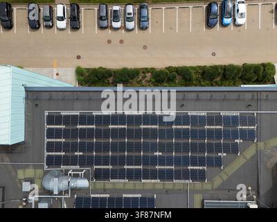 Vista aerea dall'alto di pannelli solari installati sul tetto di un edificio commerciale accanto a un parcheggio con auto, infrastruttura urbana per le energie rinnovabili Foto Stock