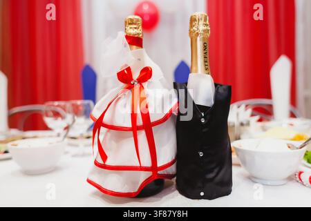 Due bottiglie di champagne vestite da sposa e sposo si trovano su un tavolo nuziale festoso. Foto Stock