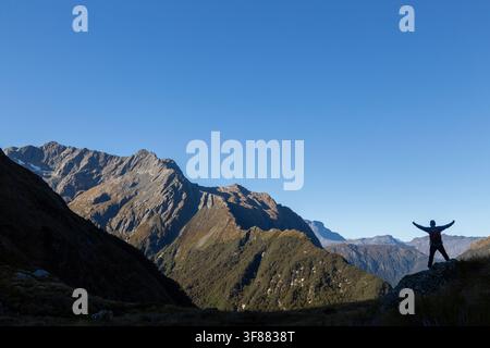 Un escursionista sul Routeburn Track che posa contro il cielo con la catena montuosa dell'Humboldt nel Parco Nazionale di Mount Aspiring, Nuova Zelanda Foto Stock