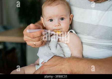 Un momento sereno di un bambino nutrito con un cucchiaio di plastica, catturato in un primo piano che evidenzia l'atmosfera calma e premurosa di un ambiente interno Foto Stock