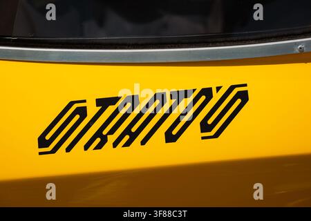 Lindau, Svizzera, 9 agosto 2026. Primo piano dettagliato di un logo adesivo geometrico nero del modello Stratos applicato sulla carrozzeria gialla brillante di un clas Foto Stock