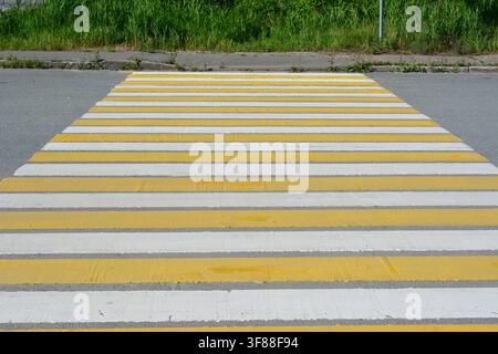 Prima piano di un passaggio pedonale a strisce gialle e bianche su una strada asfaltata Foto Stock
