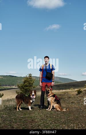 Un uomo con uno zaino e due cani viaggia nei campi nelle montagne del sud-ovest della Serbia vicino alla città di Zlatibor. Escursioni nella natura all'inizio dell'autunno Foto Stock