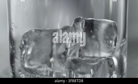 Cubetti di ghiaccio appoggiati all'interno di un bicchiere, che mostrano trasparenza e texture. La condensa aggiunge alla sensazione fredda e rinfrescante Foto Stock
