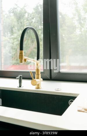 Un rubinetto da cucina moderno con acqua che gocciola in un primo piano, che mostra il suo design elegante e l'estetica pulita e contemporanea. L'oro e il nero Foto Stock