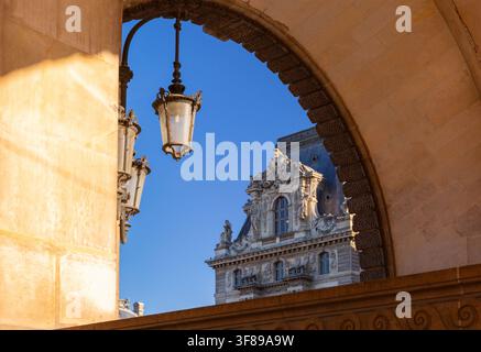 Facciata storica ornata con dettagli scultorei e lanterne sospese viste attraverso un grande arco di pietra a Parigi, Francia. Foto Stock