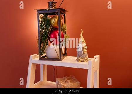 Giocattolo di Babbo Natale bianco e dorato su scaffale bianco su sfondo marrone. Palline rosse, bianche e dorate e ramo di abete nelle vicinanze. Vacanze invernali Foto Stock