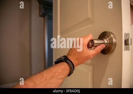 Prima di una mano di una persona che aziona una moderna maniglia da porta in nichel satinato o cromo con serratura di privacy montata su una porta a pannelli bianchi Foto Stock