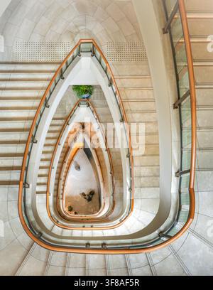 Vista dell'elegante scala a chiocciola al The Peninsula Tokyo, con gradini in pietra lucida e una ringhiera curva in legno, che guarda giù verso il luminoso Foto Stock