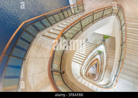 Vista dell'elegante scala a chiocciola del Peninsula Tokyo con ringhiere moderne in vetro e corrimani in legno a Chiyoda City, Tokyo, Giappone. Foto Stock
