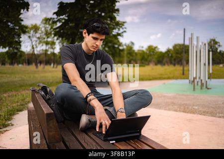 Giovane uomo che usa un tablet come laptop su una panchina del parco Foto Stock
