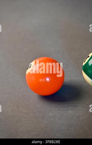 Fotografia commerciale in primo piano di una palla da biliardo arancione e di una parte di un'altra palla sul feltro grigio di un tavolo da biliardo, catturando la trama e la configurazione del gioco. Foto Stock