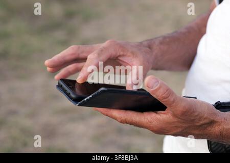 Le mani di una persona sono occupate a tenere un telefono cellulare e a usare attivamente lo schermo touch con il dito, evidenziando connessione, comunicazione e digitale Foto Stock