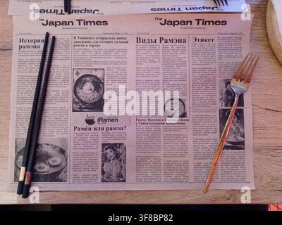 Tashkent, Uzbekistan – 06 aprile 2026 – Il giornale artificiale The Japan Times giace su un tavolo di legno con bacchette e forchetta, illustrando la cultura asiatica Foto Stock
