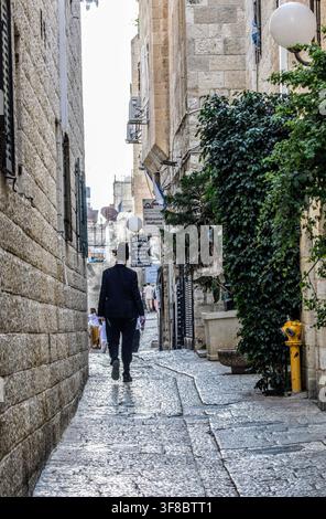 Vicolo stretto della Città Vecchia di Gerusalemme con un uomo in abito nero che si allontana Foto Stock