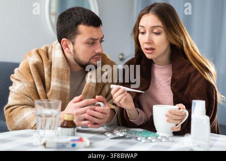 Coppia affetta da influenza e tosse seduta avvolta in coperte Foto Stock