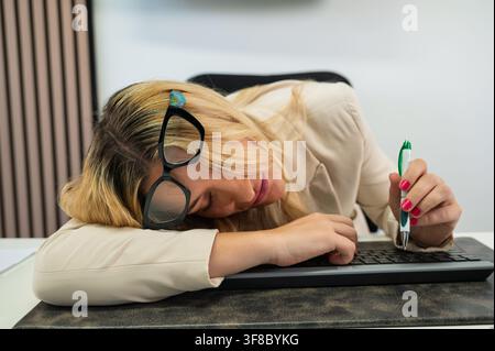 Donna d'affari che dorme sulla scrivania con occhiali e penna durante il lavoro, in preda allo stress Foto Stock