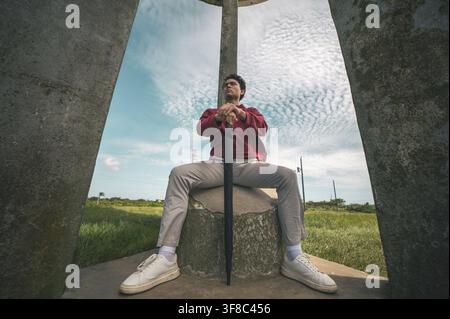 Giovane uomo seduto con le gambe divaricate, scattato da un angolo basso. Crucero - Managua, Nicaragua Foto Stock