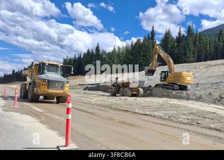 AUTOSTRADA TRANS-CANADA, CANADA – 10 LUGLIO 2026: Un escavatore pesante a cingoli scava terreno e lo carica in un camion ribaltabile articolato su un piano stradale in terra, mentre Foto Stock