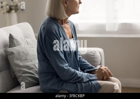 Donna anziana seduta da sola su un divano con le mani sulle ginocchia Foto Stock