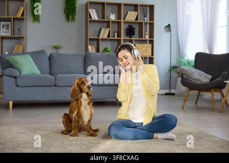 Giovane donna con cuffie e cane Cocker Spaniel che si rilassano insieme a casa Foto Stock
