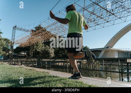 Un uomo corre all'aperto su un ponte con un corpo d'acqua sullo sfondo, ripreso da una prospettiva bassa. La scena mostra uno stile di vita attivo con abiti verdi e neri, un aspetto metallico. Foto Stock