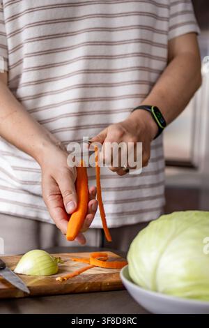 Uomo gratta le carote accanto al cavolo e ad altri ingredienti mentre prepara involtini di cavolo fatti in casa. Concetto di lavoro condiviso in cucina, preparazione del pasto, fam Foto Stock