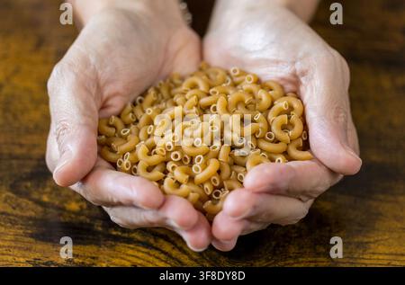 Mani che tengono pasta integrale a forma di gomito cruda Foto Stock