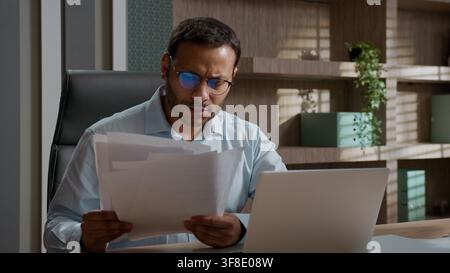 Uomo d'affari indiano-americano arrabbiato e frustrato che getta carte sulla scrivania, lavoratore stressato con laptop, uomo d'affari stanco e infelice, dipendente d'ufficio, scadenza Foto Stock
