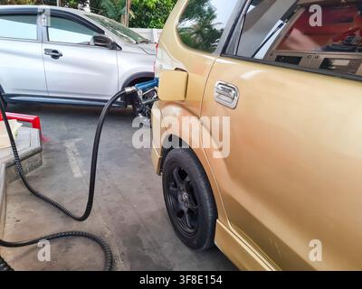 Prima di una macchina dorata che fa rifornimento in una stazione di servizio. Un erogatore di carburante è inserito nel serbatoio, evidenziando il consumo di energia e i viaggi in auto. Foto Stock