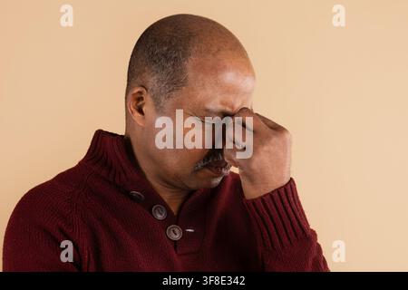 Uomo nero maturo che si pizzica il ponte del naso con gli occhi chiusi, rappresentando lo stress Foto Stock