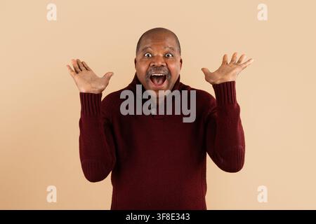 Uomo afroamericano maturo e felice che celebra con le mani alzate e un'espressione entusiasta Foto Stock
