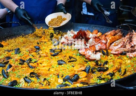 Autentica paella spagnola di frutti di mare servita da una grande padella tradizionale da paella in un mercato alimentare all'aperto o festival. Gamberetti freschi, aragosta, cozze Foto Stock
