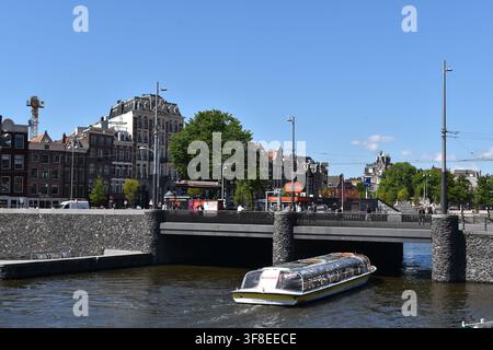 Amsterdam, Paesi Bassi – 19 maggio 2025: un battello turistico sul punto di passare sotto un ponte nel centro storico di Amsterdam, Paesi Bassi Foto Stock