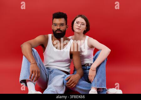 Una coppia multirazziale elegante condivide un momento caloroso su uno sfondo rosso. Foto Stock