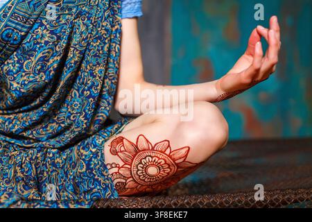 Una donna in un sari blu a motivi medita con un intricato disegno a henné sulla gamba e sulla mano. Foto Stock