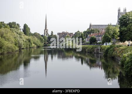 Vista della cattedrale di Worcester e del campanile di Sant'Andrea riflessi nel fiume Severn con rive lussureggianti e architettura storica a Worcester, Inghilterra Foto Stock